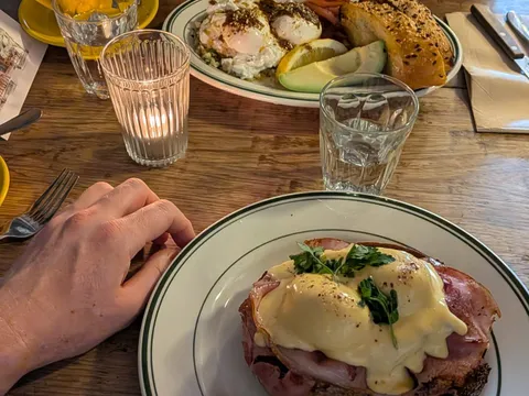 A table set for lunch, with a ham and poached egg dish, eggs on toast with avocado, and coffee.