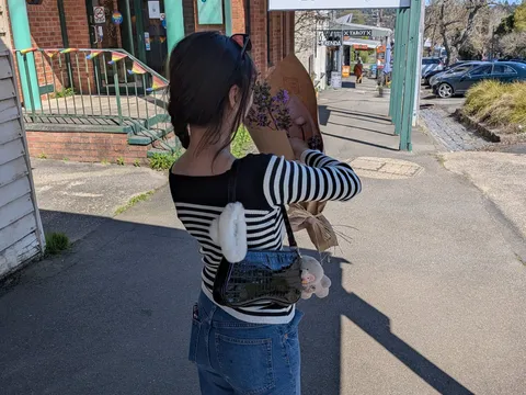 A woman walking down a Daylesford side street past old shopfronts, holding a bunch of flowers.