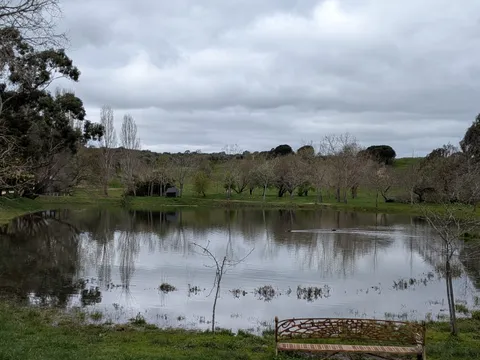A small pond on the farm under an overcast sky, with a wrought-iron bench on its bank.