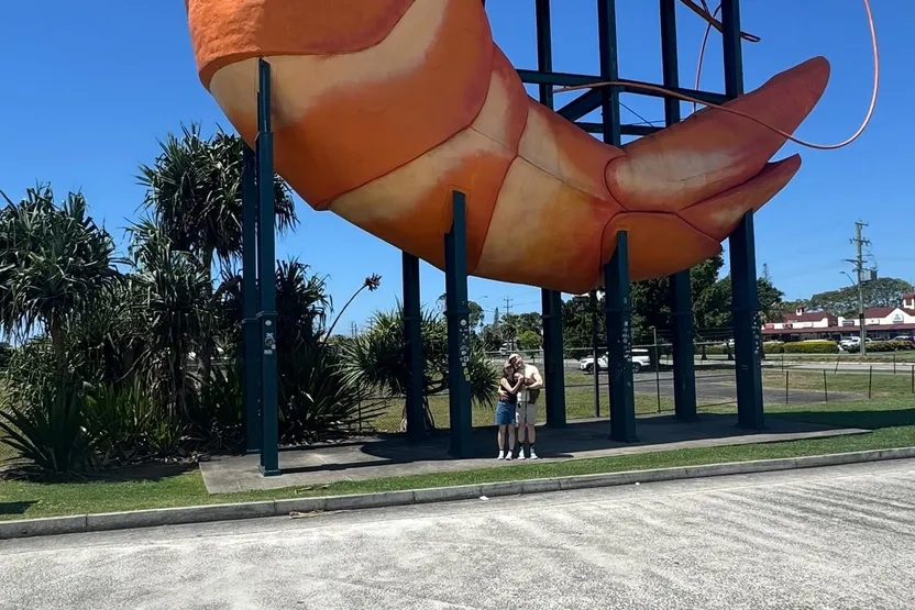 Standing beneath the big prawn, Ballina's giant roadside statue, against a clear blue sky.